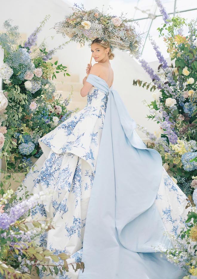 A bride in a blue and white printed wedding gown by Sareh Nouri surrounded by florals and holding an umbrella made out of flowers. 