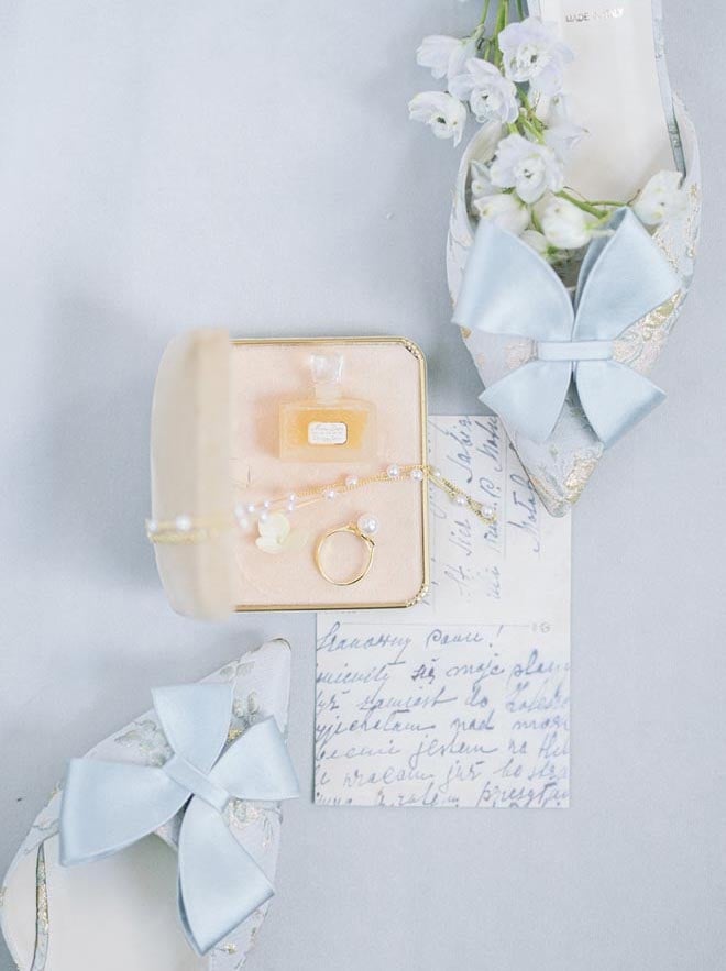 A flat lay featuring pearl jewelry, a note and blue heels. 