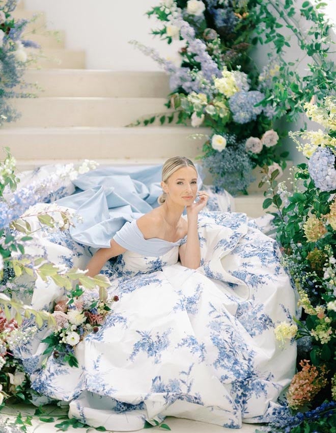 A bride in "Hydrangea" by Sareh Nouri sitting on the stairs surrounded by flowers. 