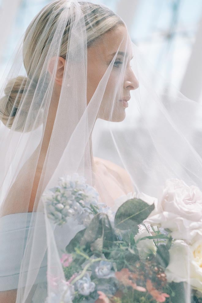 The bride holding a bouquet of flowers with the veil over her face. 