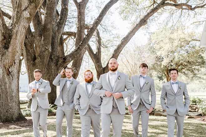 The groomsmen walk outside under oak tress at a Houston wedding venue. 