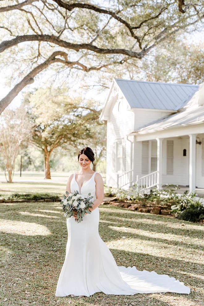 The bride looks down at her greenery and white flower wedding bouquet outside the wedding venue in Houston.