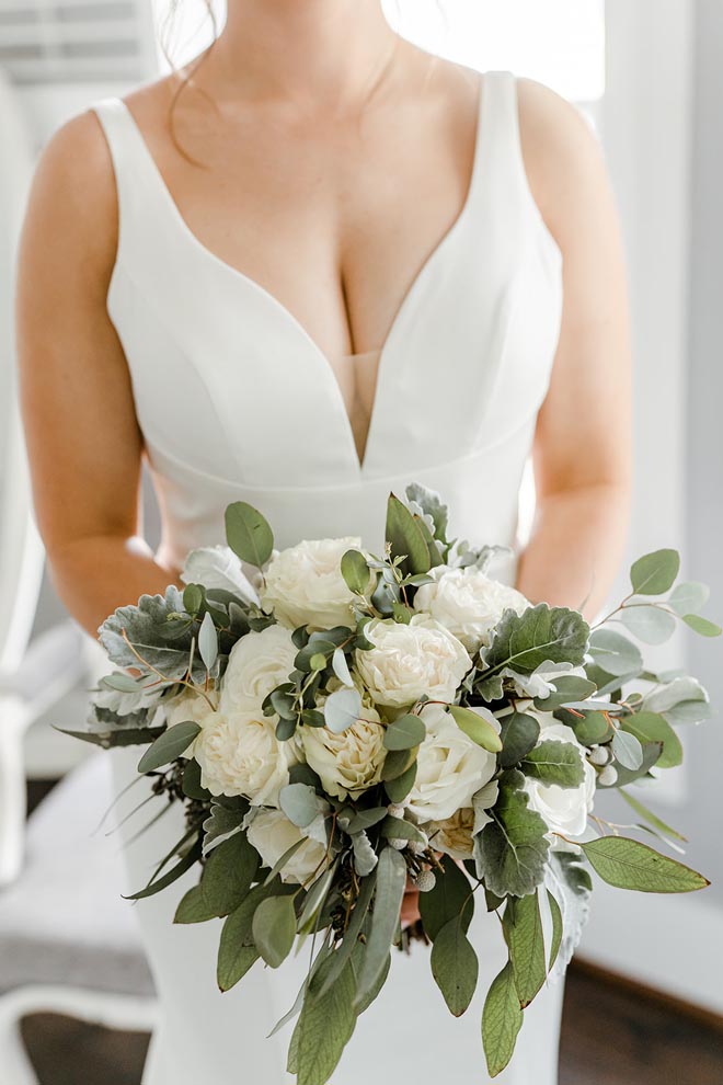 The bride holds her wedding bouquet of greenery and white flowers. 