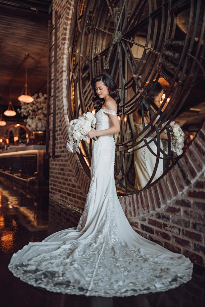 The bride stands in front of a mirrored clock at The Astorian holding her wedding bouquet. 