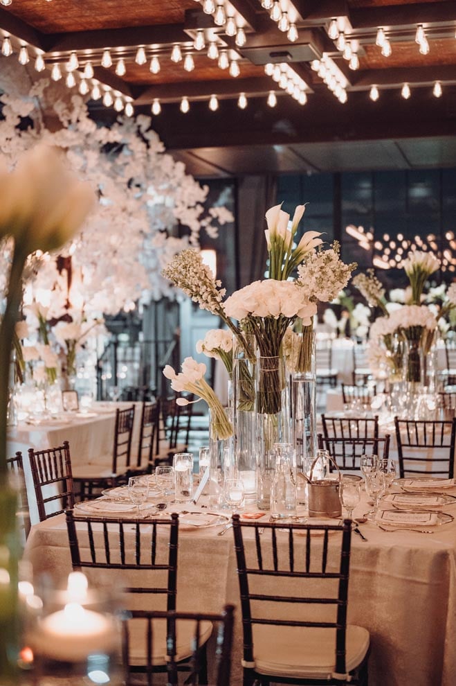 Various white florals and warm candle light adorn the reception tables at the couple's monochromatic wedding. 