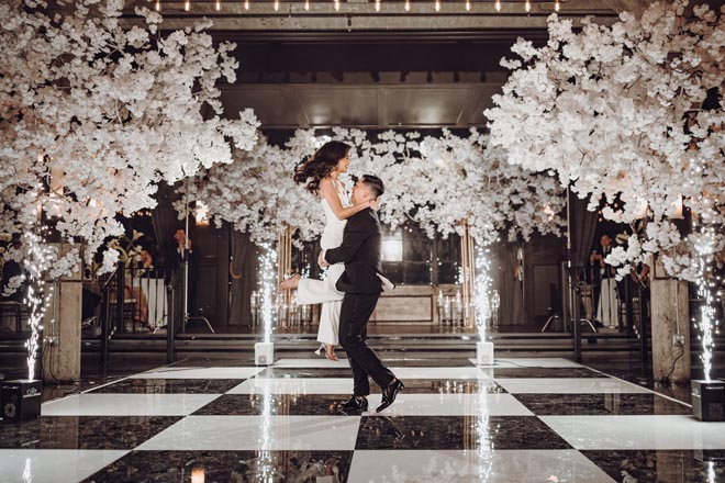 The bride and groom dance under sparklers and white floral-infused trees. 