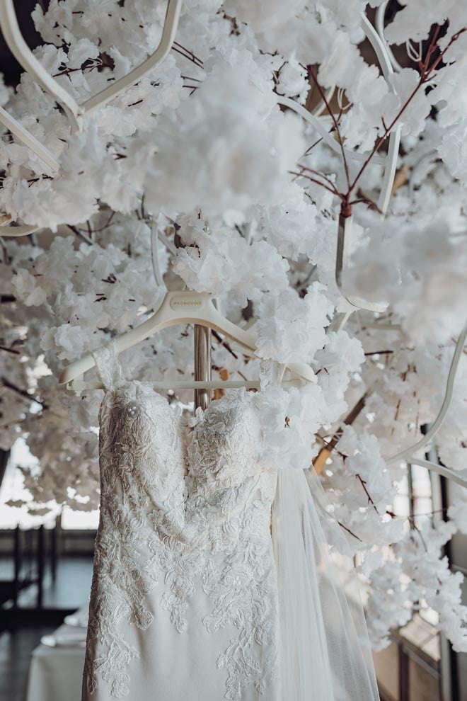 The bride's wedding gown hangs under a white floral instillation at The Astorian.
