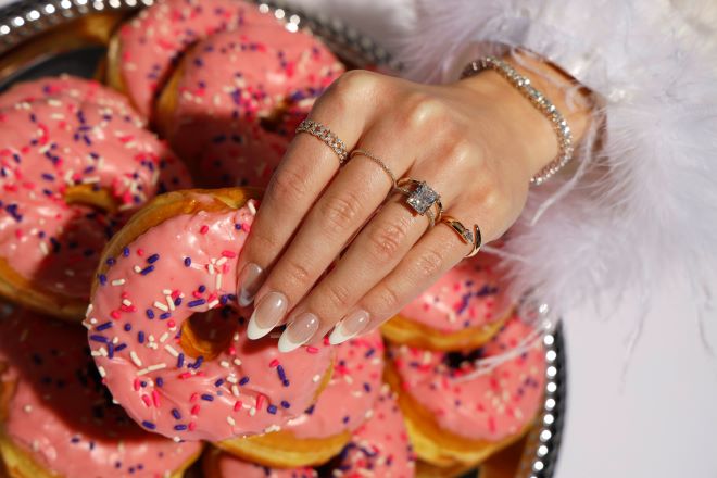 The model picks up a pink donut with sprinkles while wearing elongated diamonds from Zadok Jewelers.