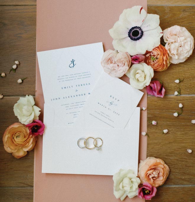 Spring colored flowers and blue and white wedding stationery lay on a wooden background.