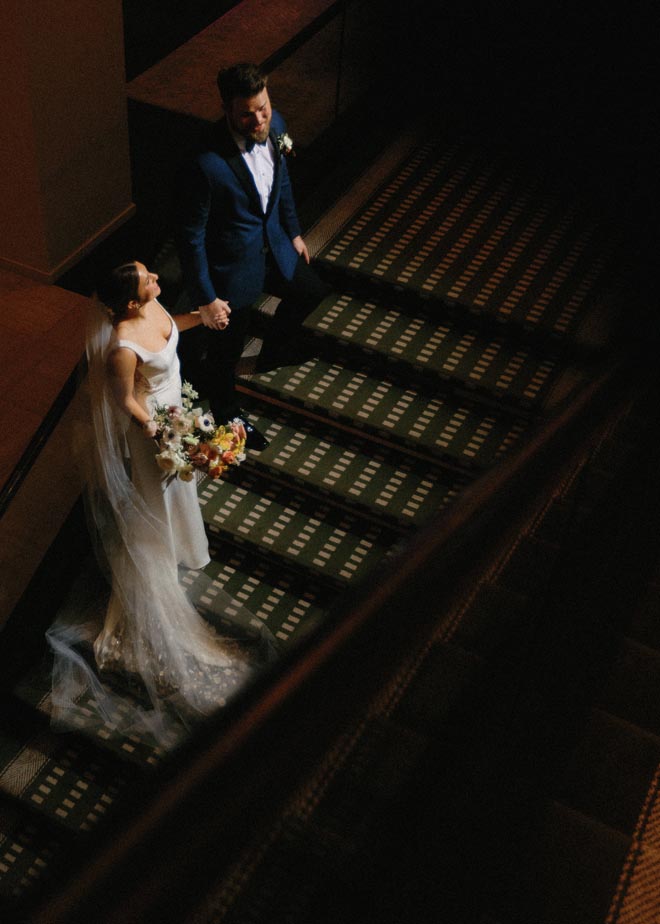 The bride and groom hold hands as they walk up the stairs at their wedding venue, the Omni Houston Hotel.