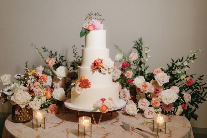 Vibrant florals adorn a 4-tier white wedding cake designed by Cakes by Gina for the springtime garden wedding. 