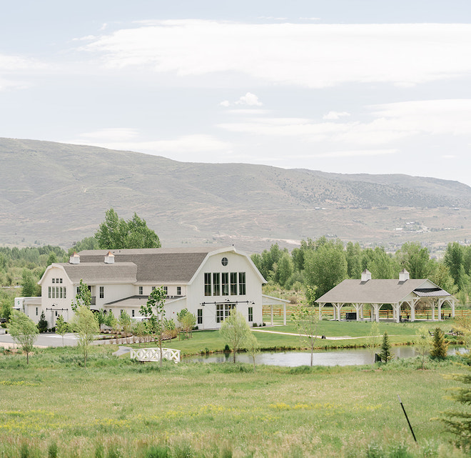 A white barn-style wedding venue in a field with mountains behind it in Park City, Utah. 