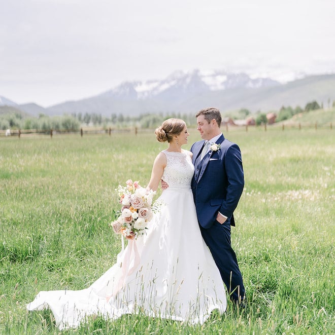 A bride and groom standing in a field with mountains behind them in Park City, Utah