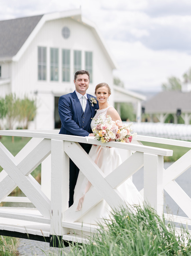 The bride and groom smiling on a bridge in front of the barn-style venue. 
