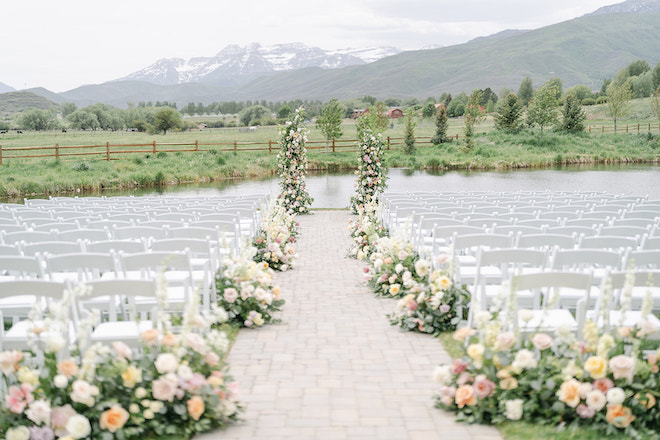 The ceremony space with white chairs lined with pink, purple and ivory florals with a floral installation as the altar with scenic mountains behind them. 