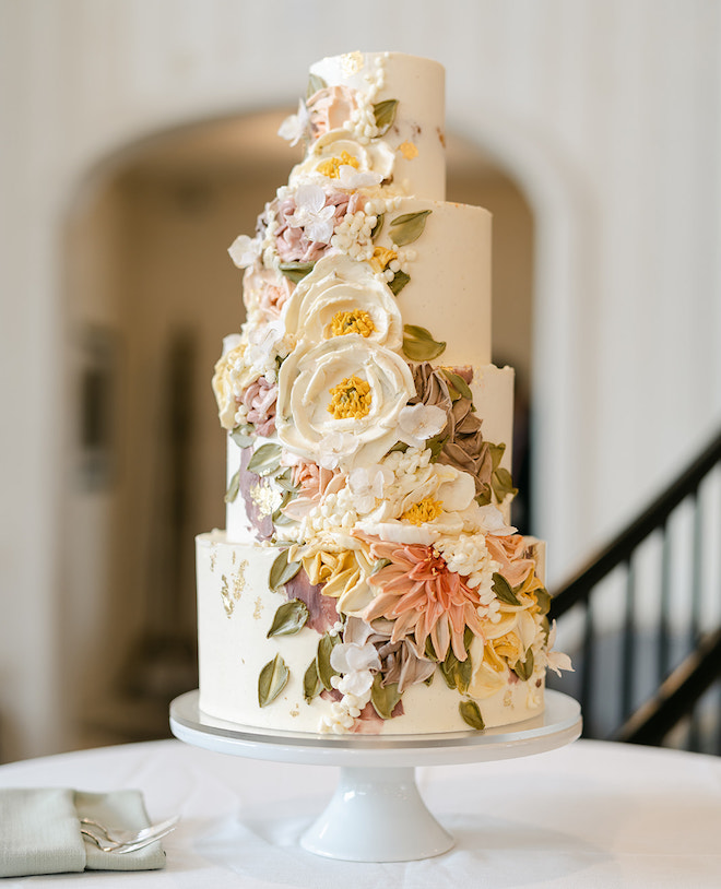 A four-tier white cake with painted white, lavender and pink florals. 