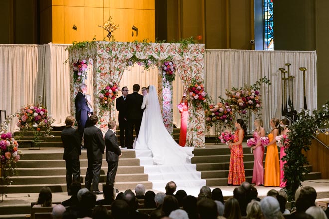 The bride and groom standing under the floral print Chuppah. 