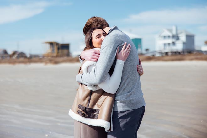 The couple hug on the beach after getting engaged. 