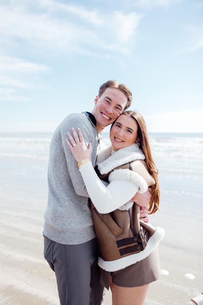 The couple smile as the celebrate their engagement on the beach. 