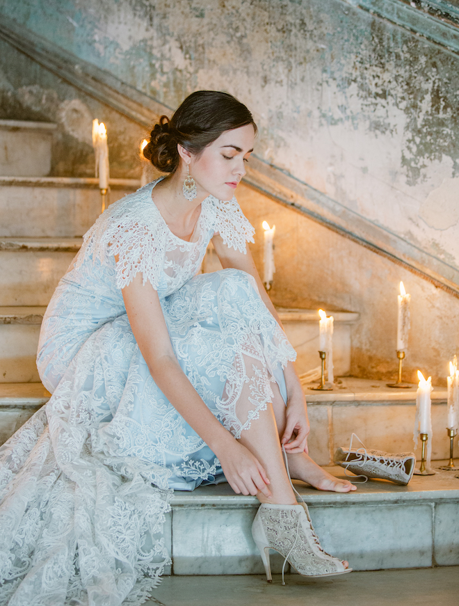 A bride sitting on candlelit stairs putting on lacy high heels. 