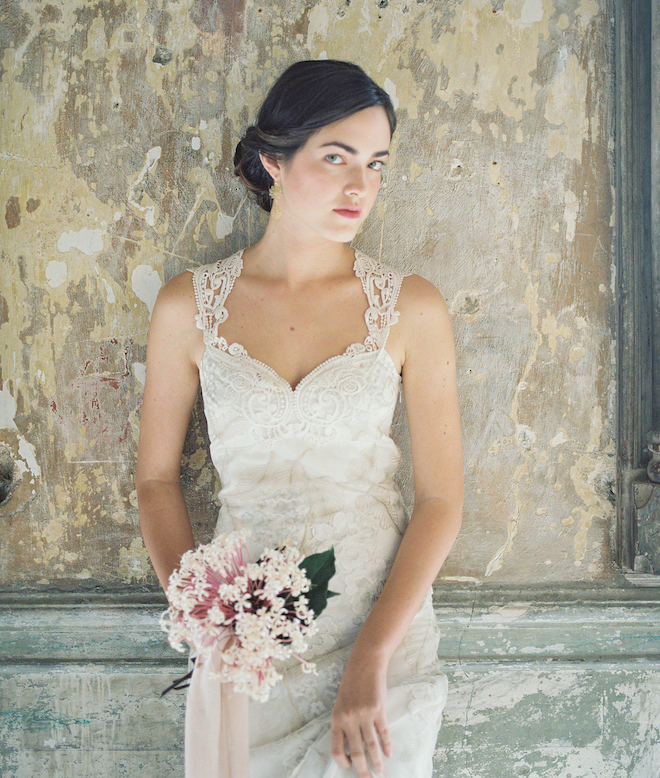 A bride wearing a sleeveless lace gown with a small floral bouquet. 