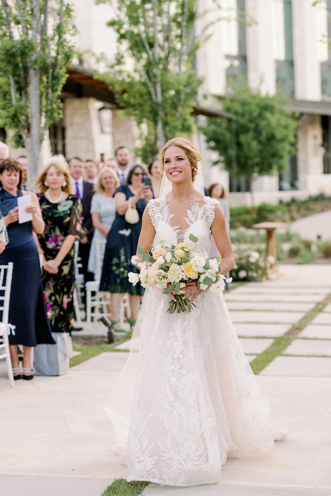 The bride walks down the aisle at her outdoor ceremony in the Texas hill country.