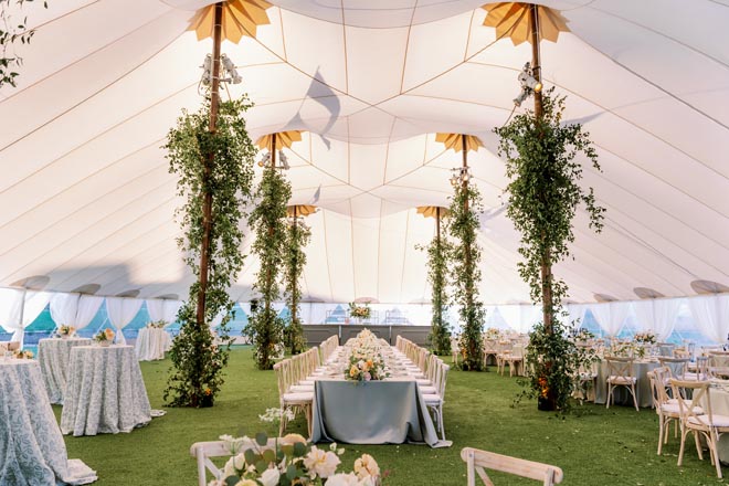 Sage, peach and orange colored decor and lush greenery decorate the outdoor wedding reception.