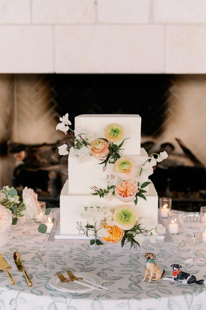 A three-tier white wedding cake with sage, peach and orange flowers. 