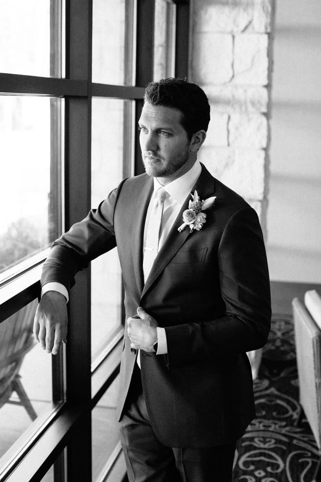 Wearing his tuxedo, the groom looks out the window at Omni Barton Creek Resort & Spa