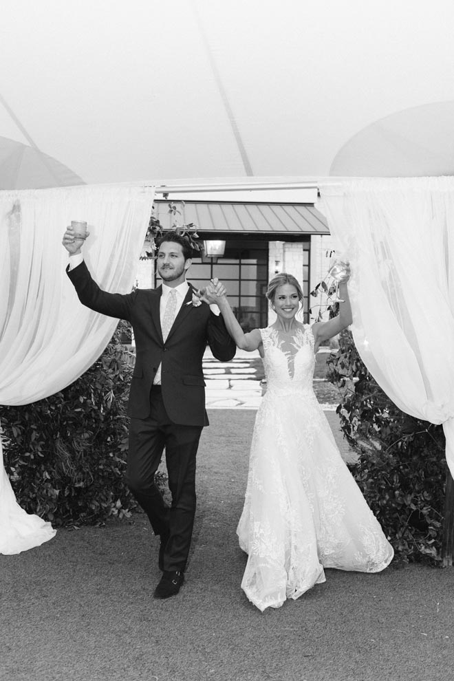 The bride and groom walk into their outdoor wedding reception holding hands. 