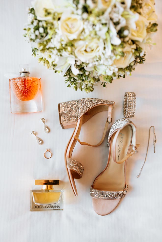 The brides shoes, perfume and wedding jewelry lay next to her wedding bouquet.