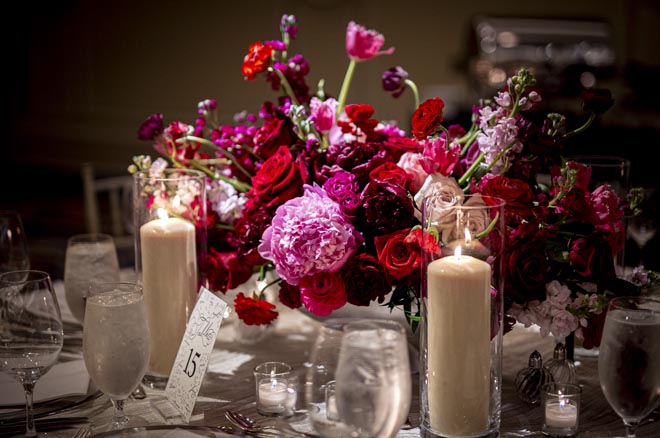 Magenta, burgundy and pink floral centerpieces decorate the wedding reception tables. 