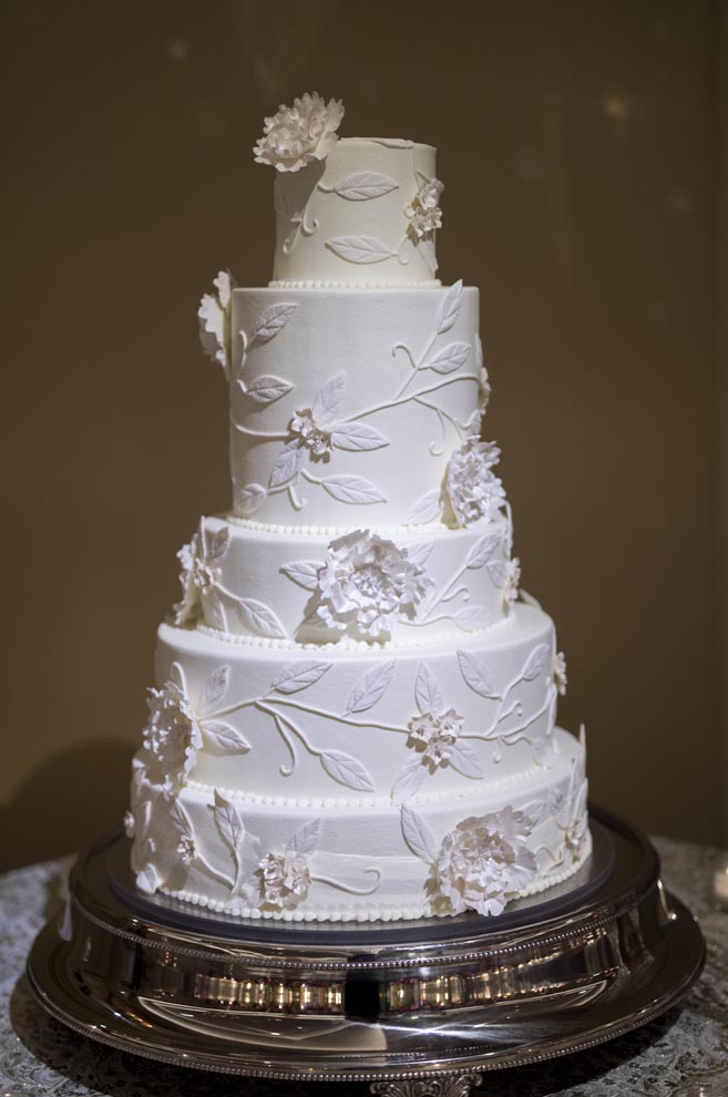 A five-tier white wedding cake designed by Susie's Cakes stands on a silver platter.