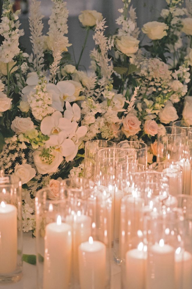 Blush, white and verdant greenery wedding florals with pillar candles detail the reception tables.