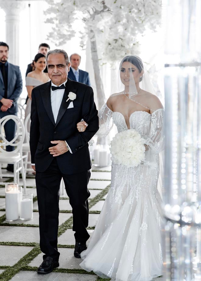 The bride and her father walk down the aisle for the black and white Persian wedding at the Sans Souci Ballroom.