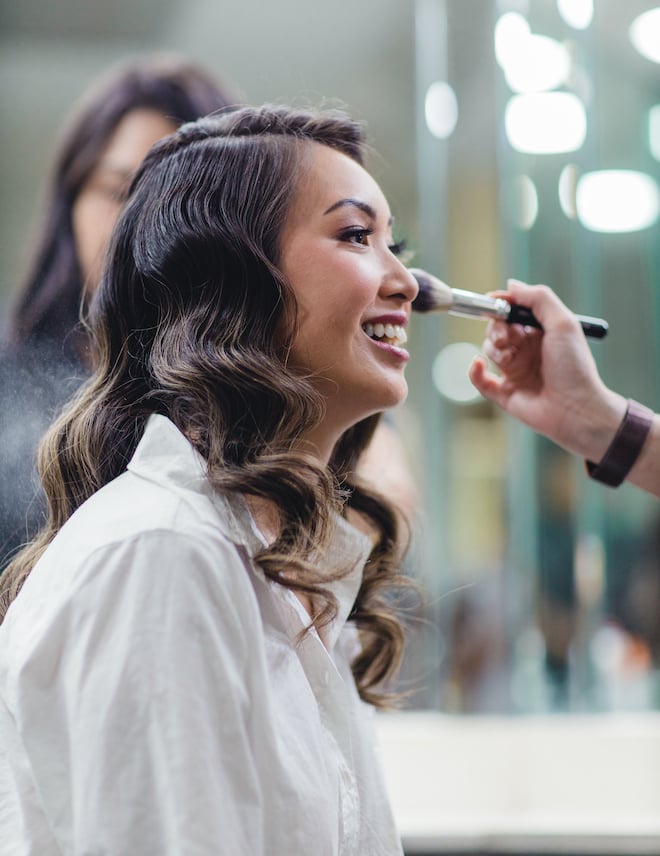 A bride smiling while getting her makeup done by Polished Makeup & Hair. 