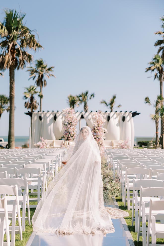 The bride walks down the mirrored aisle to the altar at her Gulf Coast pastel wedding in Galveston. 