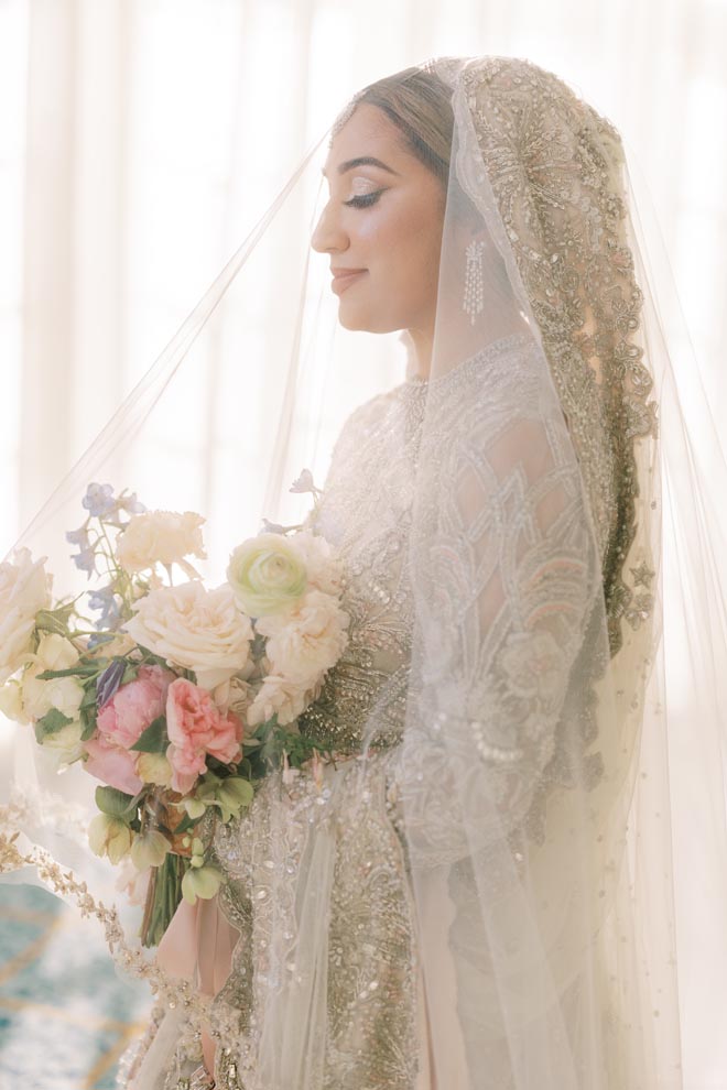 The bride wearing her veil and traditional wedding attire holds her wedding bouquet. 