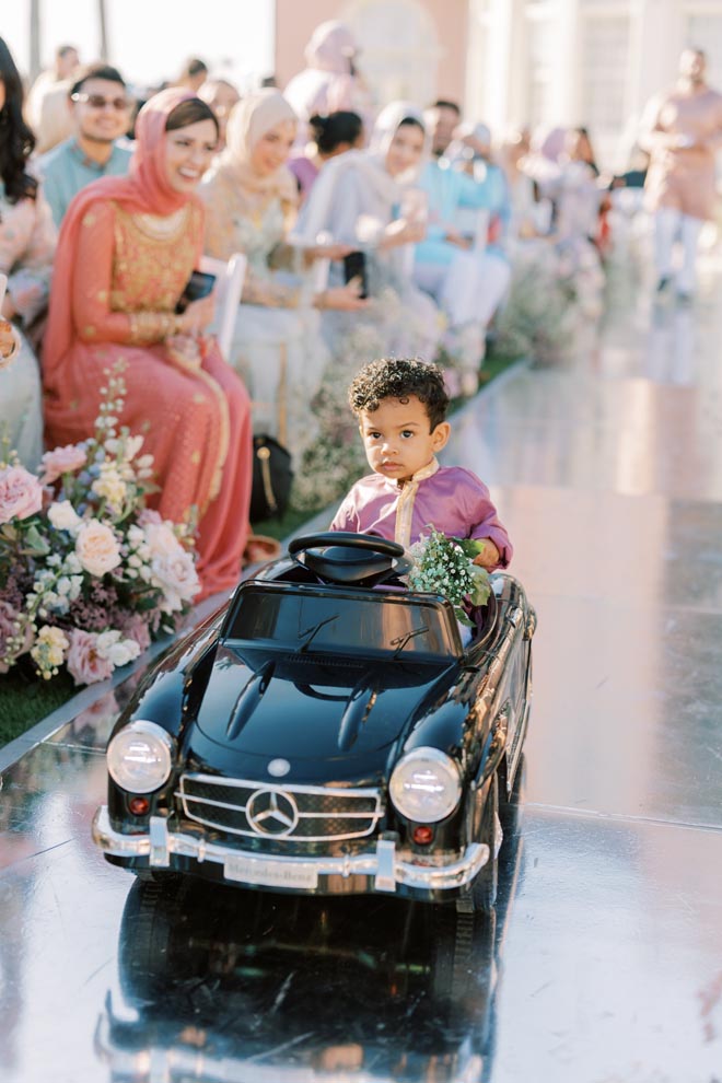 A little boy rides down the aisle in a mini Mercedes for the couple pastel Gulf Coast wedding. 