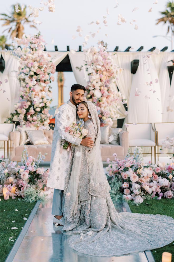 The bride and groom hug eachother in front of the altar encircled by pastel florals.