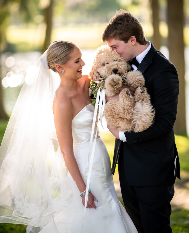 A bride and groom holding their puppy during their wedding portraits. 
