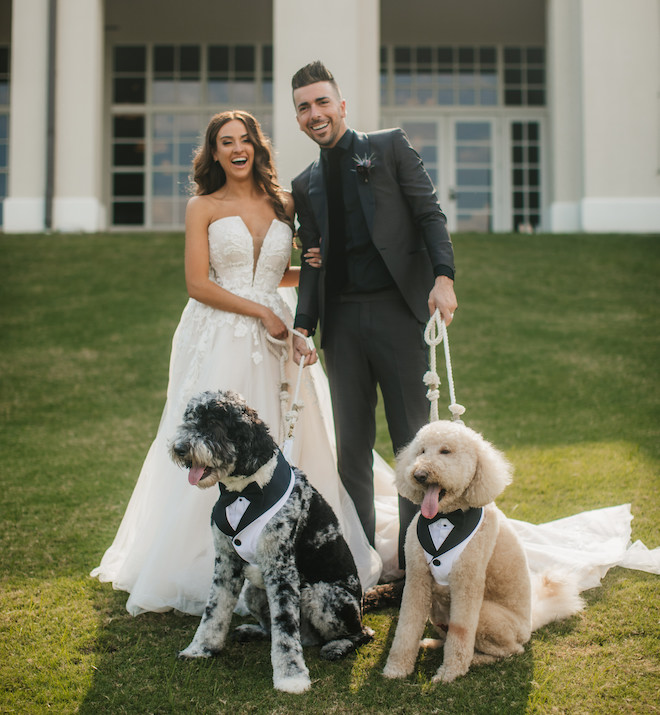 A bride and groom posing with their two dogs in front of Omni Barton Creek Resort & Spa. 