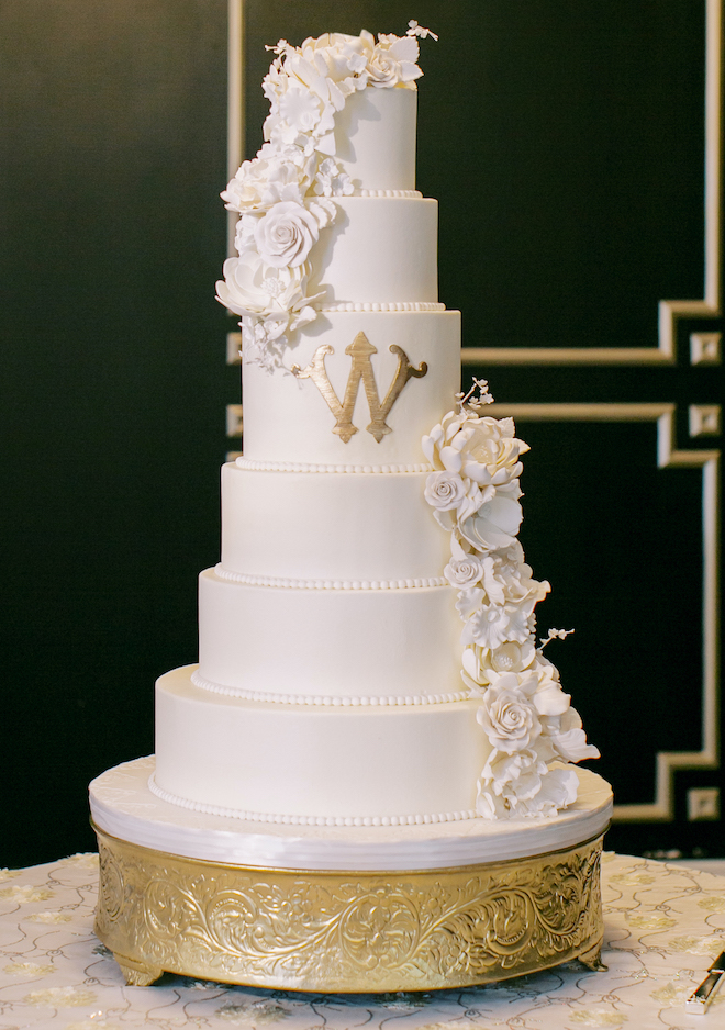 Cakes by Gina designs a six-tiered elegant white wedding cake detailed in white roses.