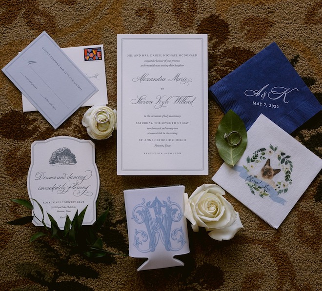 A blue and white invitation suite with a napkin with a print of a brown cat reading "Cheers!"