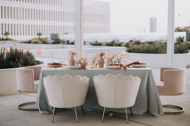 A table with a sage green tablecloth and peach toned table decor on the covered rooftop of POST Houston. 