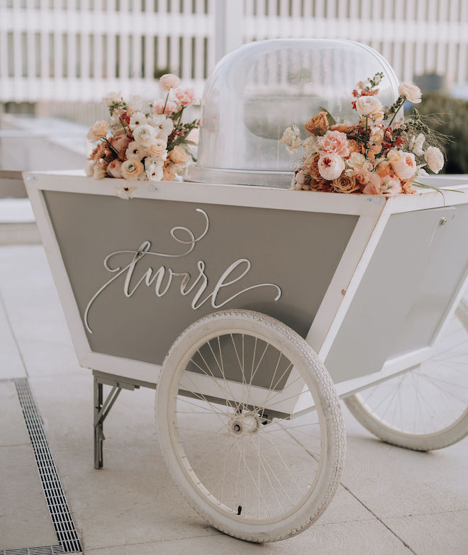A gray cotton candy cart with peach-toned florals and the world "Twirl" written in silver on the cart. 