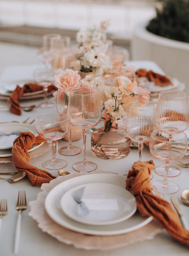 Tablescape decor with white plates, peach glassware and orange napkins. 
