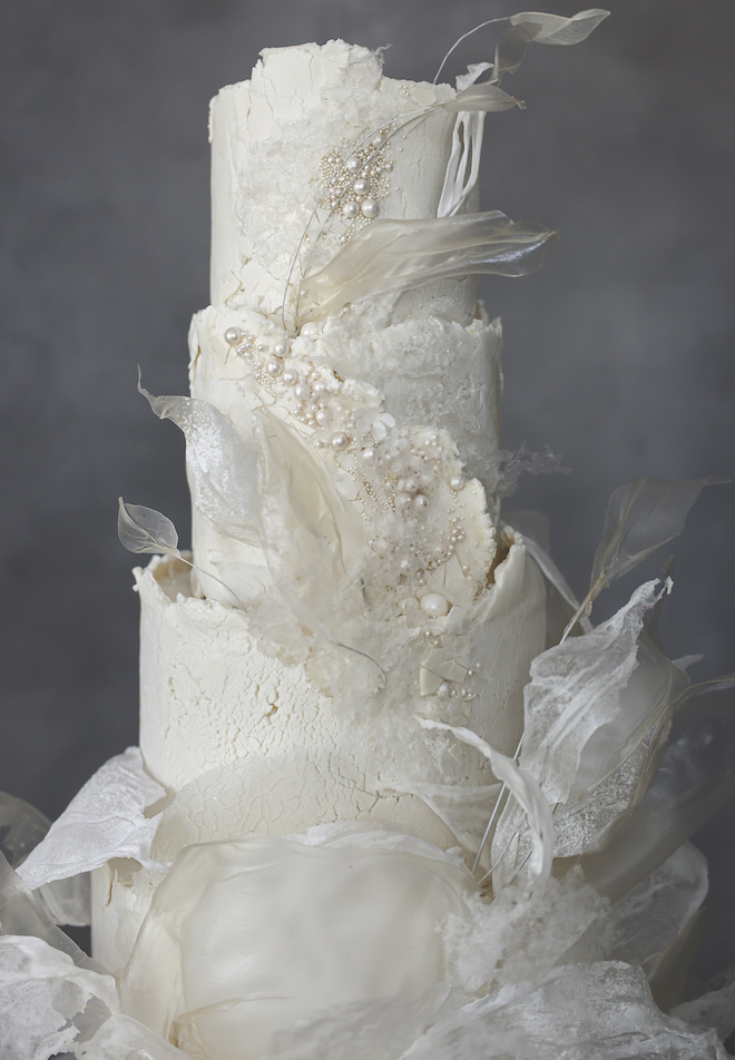 An elegant white wedding cake is decorated in tulle, textured frosting and pearls. 