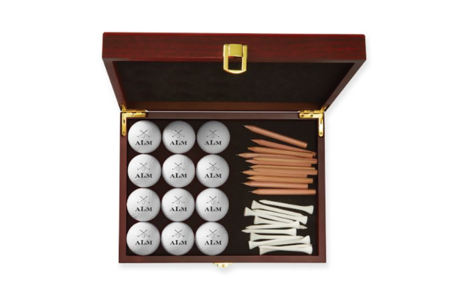 A brown wood box with gold hardware with monogrammed golf balls, white tees and brown pencils. 
