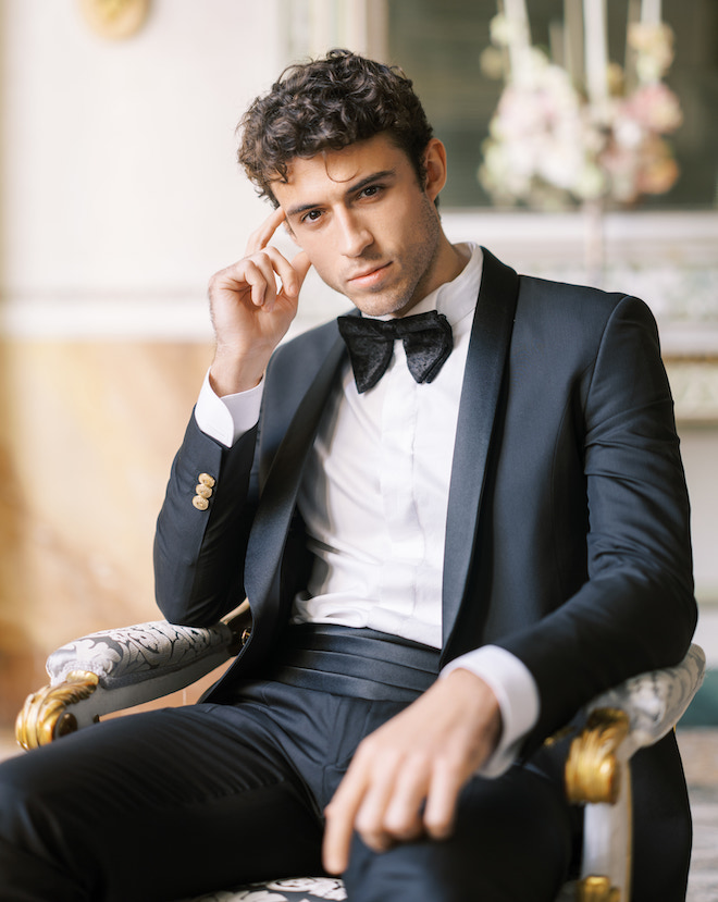 A man posing in a chair wearing a tuxedo.